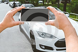 Close-up, Mockup of a smartphone in the hands of a man. Against the background of a white electric car in the city