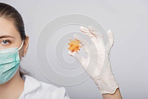 Close-up model of coronavirus in the hands of a doctor. A young woman in a white coat, mask and gloves studies the virus.