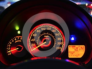 Close up modern car`s dashboard with speedometer fuel indicator temperature light and tachometer at night.