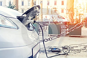 Close-up modern electric car pugged with fast charger at charging station in center of old European city. Ecol friendly green