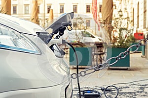 Close-up modern electric car pugged with fast charger at charging station in center of old European city. Ecol friendly green