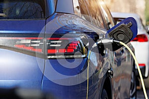 Close-up modern electric plug-in hybrid car parked near fast charger charging station point in center street old