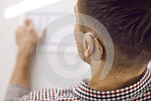 Close-up of modern model of hearing aid tucked into ear of unrecognizable young man.