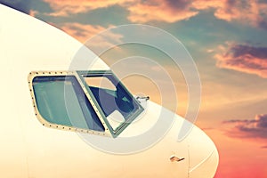 Close-up modern passenger commercial airplane cockpit flying against colorful dramatic sunset sky. Detail side view of