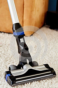 Close up of modern vacuum cleaner on beige carpet on floor in living room, copy space. Housework, household, spring-cleaning.