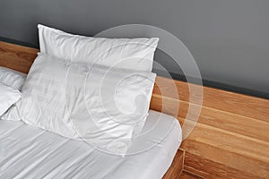 Close-up modern white bed, wooden bedhead and gray wall