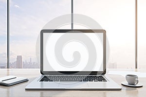 Close up of modern wooden desktop with empty white mock up laptop screen, supplies, coffee cup and panoramic window with city view