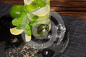 A close-up of a mojito cocktail on a black plate. Green mojito on a wooden background. Green mint, pieces of lime and ice cubes.