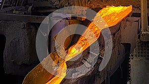 Close-up of molten metal flowing in factory. Stock footage. Beautiful molten substance flows down drain at steel plant
