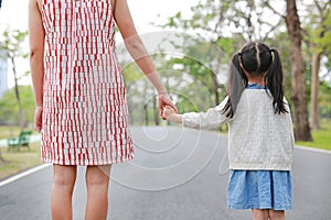 Close-up mom and daughter holding hands in the outdoor nature garden. Back view