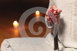 A close-up of the monk`s hands hold red rosaries against the background of the wooden floor of the practice room and lit