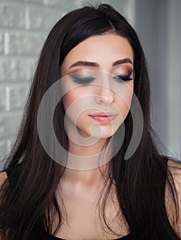 Close up mood portrait of young beautiful woman with gorgeous long brunette hair showing trendy facial makeup indoors