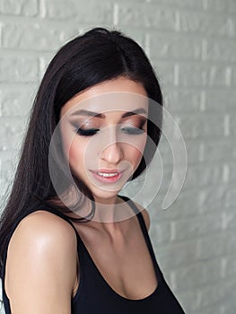 Close up mood portrait of young beautiful woman with gorgeous long brunette hair showing trendy facial makeup indoors