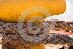 Close-up of a mooring rope with a knotted end tied around a cleat on a wooden pier