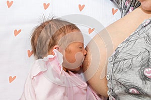 Close up mother breastfeeding her newborn child on a bed with a heart in a bright room. Mother breastfeeding her baby with breast