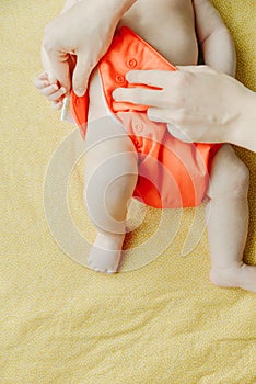 Close up of mother hands put on a baby orange diaper to her newborn