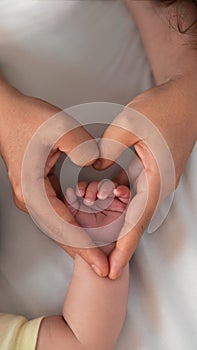Close up mother holding hands newborn boy and giving heart signal in a room