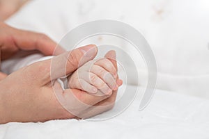 Close up mother holding tiny hand of little newborn baby boy girl, helping hands, bonding different generations. Happy