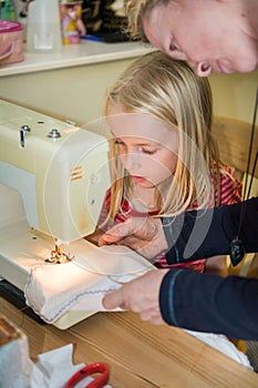 Close up of a mother teaching young daughter to use a sewing machine