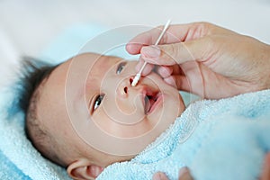 Close-up mother use cotton bud to clean infant nose. Baby Healthcare concept