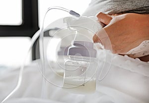 Close-up mother using automatic breast pump on the bed