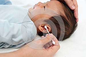 close up mother using cotton bud to cleaning ear of newborn baby on bed