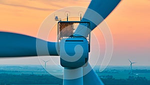 Close up of motor on wind turbine with orange sunset aerial of wind farm