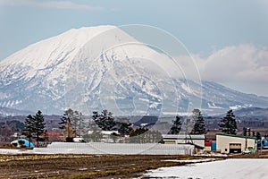 Close up Mount Yotei inactive stratovolcano with village on the foot hill and snow cover on the ground in winter in Hokkaido