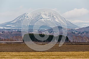 Close up Mount Yotei inactive stratovolcano with village on the foot hill and yellow grass on the ground in winter in Hokkaido