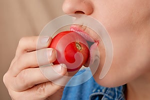 Close-up of the mouth of a pretty Caucasian woman biting a fresh raw tomato. Side view from low angle