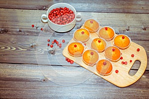 Close-up of a muffin freshly baked decorated with red berries on a light gray wooden table top on a cutting board