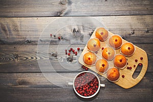 Close-up of a muffin freshly baked decorated with red berries on a light gray wooden table top on a cutting board