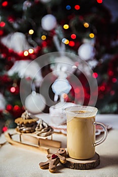 Close-up mug with coffe and milk on a wooden table, gingerbread house and christmas lights and decorations on bokeh