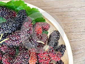 Close up of mulberry with a green leaves on the wooden plate on wooden table. Mulberry this a fruit and can be eaten in have a red