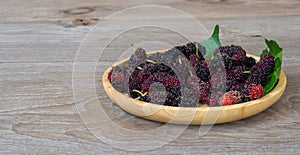 Close up of mulberry with a green leaves on the wooden plate on wooden table.This a fruit and can be eaten in have a red and purpl