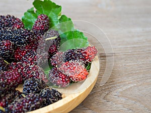 Close up of mulberry with a green leaves on the wooden plate on wooden table. Mulberry this a fruit and can be eaten in have a red