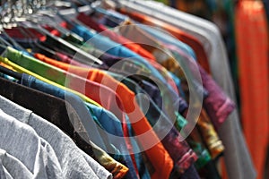 Close-up of multi-colored T-shirts hanging on hangers in the street, fair, secondhand, recycling concept