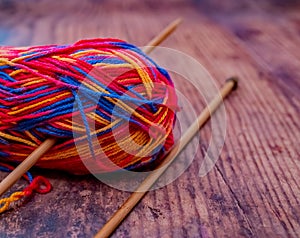 Close up of a multi coloured ball of knitting yarn and bamboo knitting needles on a wooden floor