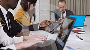 Close-up of multi-ethnic group of young business people sitting at the table on conference and working on computer