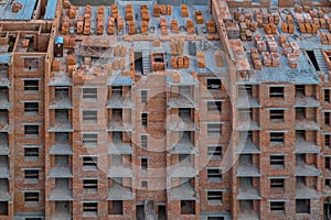 Close-up on a multi-storey residential building under construction from red brick with a part of a crane. The walls of the house