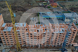 Close-up on a multi-storey residential building under construction from red brick with a part of a crane. The walls of the house