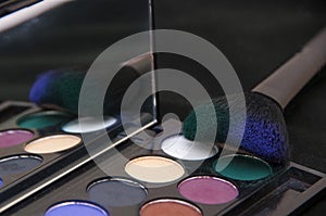 Close up of a multicolored eye shadow and a brush for applying makeup. Beauty products on the black background.