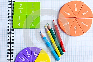 Close up of Multicolored math fractions, pencils on the open notepad on gray wooden table. Interesting math for kids background.