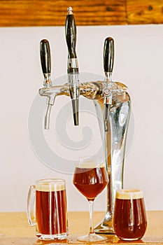 Close up of multiple beer taps located over a wooden table with some glasses full of beer, in a blurred background