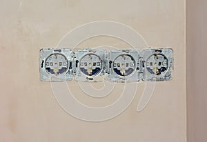 A close-up of a multiple outlet receptacle, electrical socket without a cover plate installed unevenly, badly on a plastered wall