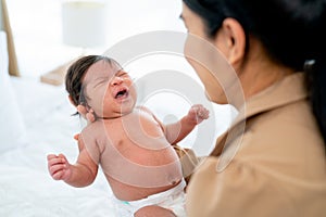 Close up multiracial newborn baby is crying and held by mother in room with day light and take care also look with love and