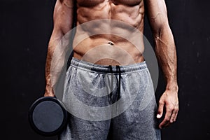 Close up of muscular bodybuilder guy doing exercises with weights over black background