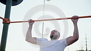 Close up of muscular man doing pull-ups on horizontal bar. On workout area near house