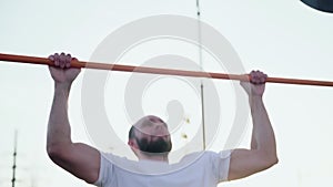 Close up of muscular man doing pull-ups on horizontal bar. On workout area near house