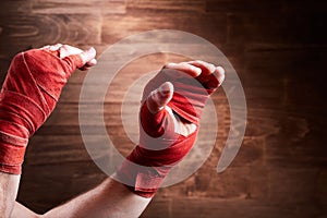 Close-up of the muscular man`s hands with red bandage against wooden wall.